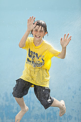 Germany, Boy jumping in splash of water against blue background - MAEF003428