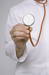 Close up of doctor holding stethoscope against grey background - TCF001572