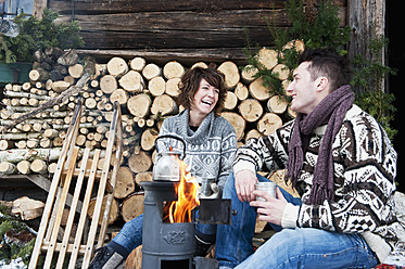 Österreich, Salzburger Land, Flachau, Junger Mann und Frau kochen Tee und sitzen am Ofen im Winter - HHF003635
