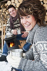 Austria, Salzburg Country, Flachau, Young man and woman making tea and sitting besides stove in winter - HHF003636