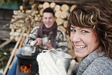 Austria, Salzburg Country, Flachau, Young man and woman making tea and sitting besides stove in winter - HHF003637