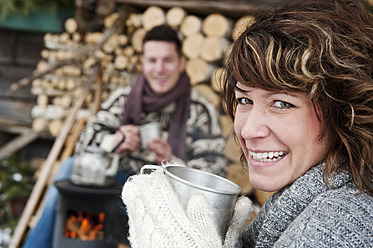 Österreich, Salzburger Land, Flachau, Junger Mann und Frau kochen Tee und sitzen am Ofen im Winter - HHF003637
