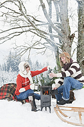 Austria, Salzburg Country, Flachau, Young man and woman making tea and sitting besides stove in winter - HHF003642