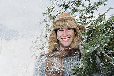 Österreich, Salzburger Land, Flachau, Junger Mann trägt Weihnachtsbaum im Schnee - HHF003650