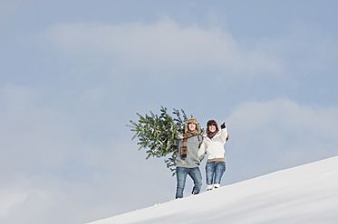 Österreich, Salzburger Land, Flachau, Junger Mann und Frau tragen Weihnachtsbaum im Schnee - HHF003652