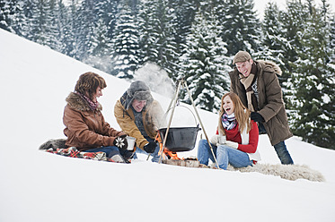 Austria, Salzburg Country, Flachau, Young men and women sitting near fireplace and making tea in snow - HHF003661