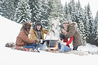 Austria, Salzburg Country, Flachau, Young men and women sitting near fireplace and making tea in snow - HHF003662