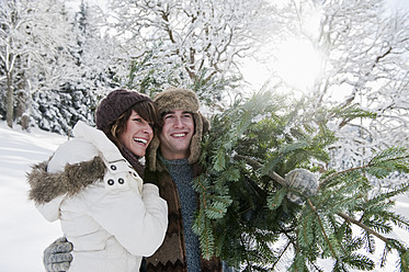 Österreich, Salzburger Land, Flachau, Junger Mann und Frau tragen Weihnachtsbaum im Schnee - HHF003670