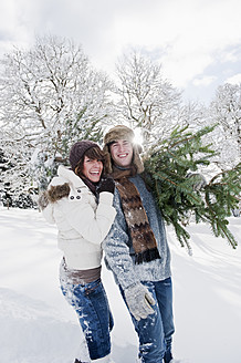Austria, Salzburg Country, Flachau, Young man and woman carrying christmas tree in snow - HHF003671