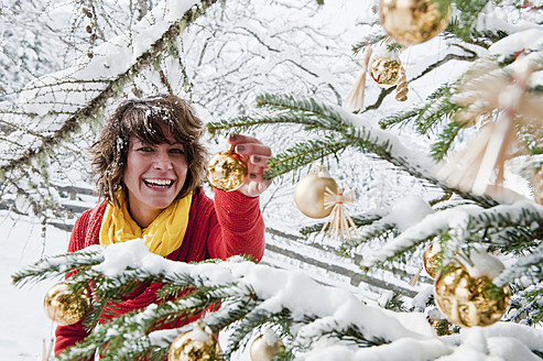 Österreich, Salzburger Land, Flachau, Junge Frau schmückt Weihnachtsbaum im Winter - HHF003673