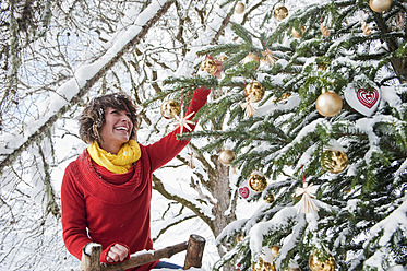 Österreich, Salzburger Land, Flachau, Junge Frau schmückt Weihnachtsbaum im Winter - HHF003674