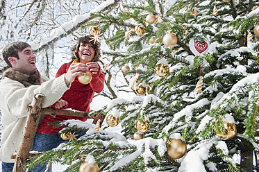 Österreich, Salzburger Land, Flachau, Junger Mann und Frau schmücken Weihnachtsbaum im Winter - HHF003675