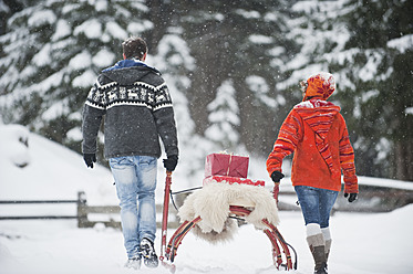 Österreich, Salzburger Land, Flachau, Junger Mann und Frau tragen Weihnachtspakete auf Schlitten im Schnee - HHF003680