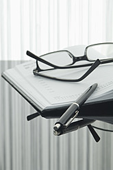 Close up of notebook, pen and spectacles with reflection on table - ASF004375