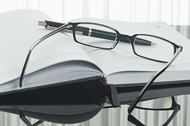 Close up of notebook, pen and spectacles with reflection on table - ASF004377