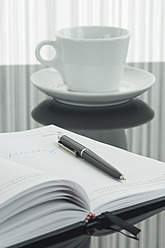 Close up of notebook, pen and coffee cup with reflection on table - ASF004380