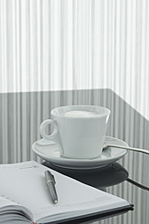 Close up of notebook, pen and coffee cup with reflection on table - ASF004381