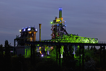 Deutschland, Nordrhein-Westfalen, Duisburg, Landschaftspark Duisburg-Nord, Blick auf beleuchteten Hochofen und Schornsteine einer alten Industrieanlage - FOF003420