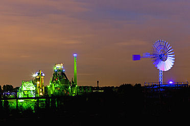 Deutschland, Nordrhein-Westfalen, Duisburg, Landschaftspark Duisburg-Nord, Blick auf beleuchteten Hochofen und Windmühle einer Industrieanlage bei Nacht - FOF003423