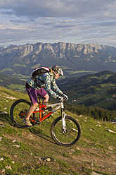 Austria, Tyrol, Spitzstein, Young woman mountainbiking on slope with Kaiser mountains in background - FFF001205