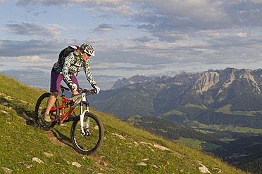 Austria, Tyrol, Spitzstein, Young woman mountainbiking on slope with Kaiser mountains in background - FFF001206