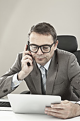 Close up of businessman with tablet pcand mobile phone against grey background - MAEF003460