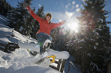 Austria, Salzburg Country, Flachau, Young woman wearing snow shoes jumping in snow - HHF003698