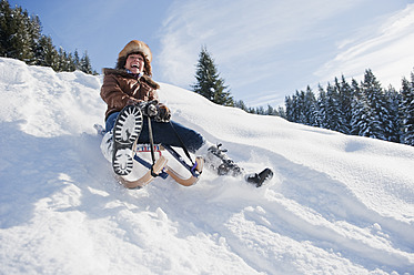 Austria, Salzburg Country, Flachau, Young woman tobogganing in snow - HHF003703