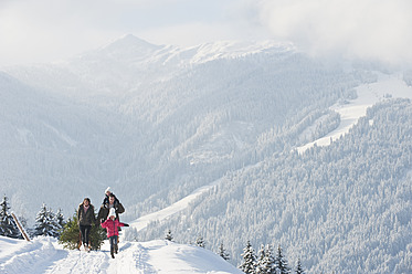 Österreich, Salzburger Land, Flachau, Blick auf Familie mit Weihnachtsbaum und Schlitten im Schnee - HHF003716