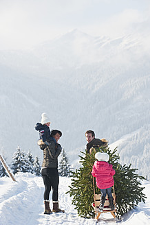 Österreich, Salzburger Land, Flachau, Blick auf Familie mit Weihnachtsbaum und Schlitten im Schnee - HHF003717