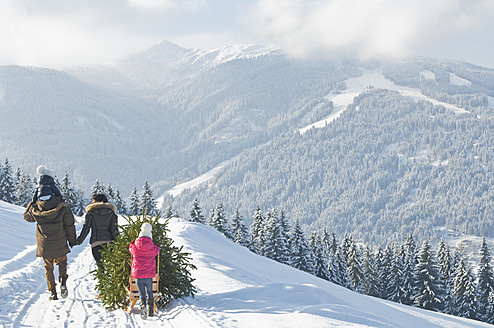 Österreich, Salzburger Land, Flachau, Blick auf Familie mit Weihnachtsbaum und Schlitten im Schnee - HHF003719