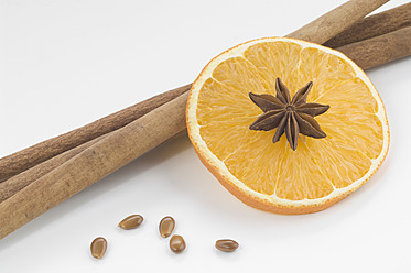 Close up of orange slice with star anise and cinnamon against white background - CRF002074