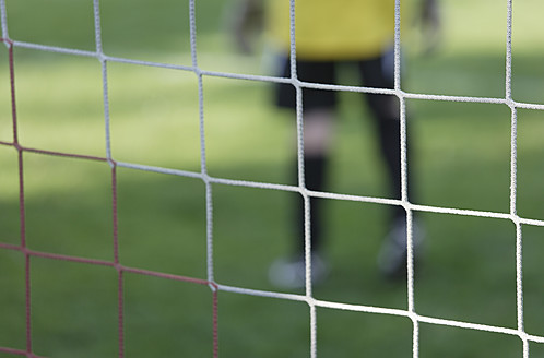 Germany, Bavaria, Schaeftlarn, Close up of football net with teenage boy goalkeeper in background - TCF001607