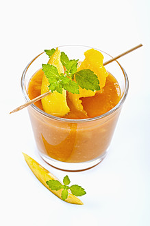 Close up of mango smoothie with mint and mango slice on white background - TSF000319