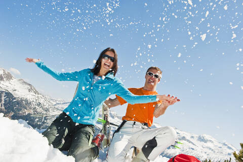 Österreich, Salzburger Land, Altenmarkt-Zauchensee, Mid adult couple sitting in winter snow and having fun, lizenzfreies Stockfoto