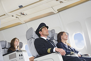 Germany, Bavaria, Munich, Mid adult flight personnels and stewardess resting in business class airplane cabin - WESTF016811