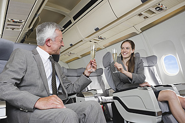 Deutschland, Bayern, München, Geschäftsmann und Frau stoßen mit Champagner in der Business-Class-Flugzeugkabine an, lächelnd - WESTF016829