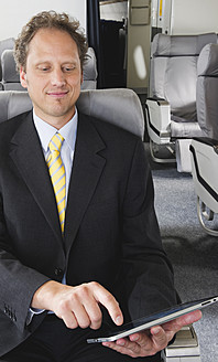 Germany, Bavaria, Munich, Businessman using ipad in business class airplane cabin, smiling - WESTF016878