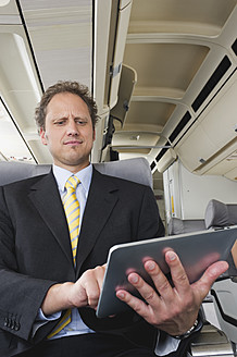 Germany, Bavaria, Munich, Businessman using ipad in business class airplane cabin - WESTF016833