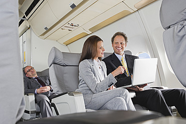 Germany, Bavaria, Munich, Businessman and businesswoman working on laptop in business class airplane cabin - WESTF016845