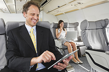 Deutschland, Bayern, München, Geschäftsleute arbeiten an ipad und Laptop in der Business-Class-Flugzeugkabine, lächelnd - WESTF016850