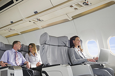 Germany, Bavaria, Munich, Business people talking and using laptop in business class airplane cabin, smiling - WESTF016857