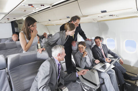 Deutschland, Bayern, München, Gruppe von Passagieren, die in der Business-Class-Flugzeugkabine in den Laptop schauen, lächelnd, lizenzfreies Stockfoto