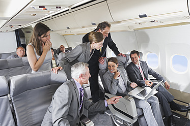 Germany, Bavaria, Munich, Group of passengers looking in laptop in business class airplane cabin, smiling - WESTF016869