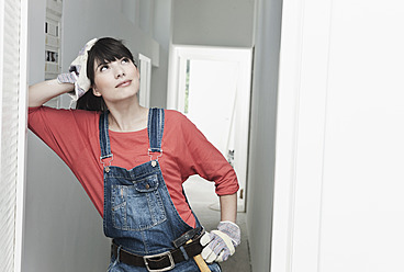 Deutschland, Köln, Junge Frau mit Hammer an Wand gelehnt beim Renovieren einer Wohnung - FMKF000251