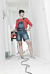 Germany, Cologne, Young woman with electric drill for renovation in corridor - FMKF000255