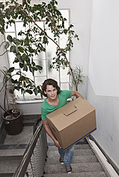 Deutschland, Köln, Junger Mann trägt Karton auf Treppe bei Wohnungsrenovierung - FMKF000261