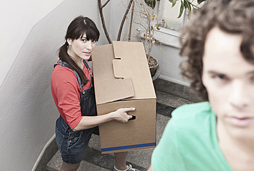 Germany, Cologne, Young couple carrying carton on stairway in renovating apartment - FMKF000283