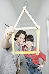 Germany, Cologne, Young couple holding house model pocket ruler in front of them - FMKF000309