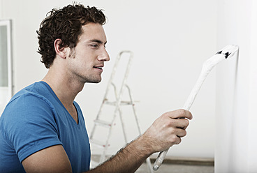 Germany, Cologne, Close up of young man painting in renovating apartment - FMKF000327